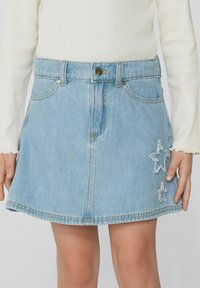 Jupe en jean bleu clair avec un design évasé, des poches avant, une fermeture à boutons et des accents d'étoiles blanches brodées sur l'ourlet.