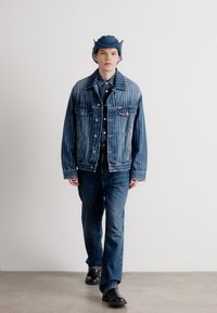 Dongerijakke med vertikale striper, mørkeblå skjorte, matchende jeans og en blå cowboylue; svarte støvler; glatt tekstur.