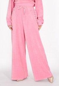 Roze wijde broek van zachte stof, met een elastische tailleband en decoratieve zilveren studs aan de zijkanten, inclusief zichtbare stiknaden.