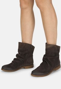 Botas de tobillo de ante marrón con un diseño holgado, que cuentan con una cremallera lateral, suela plana y detalles texturizados cerca del dedo del pie.