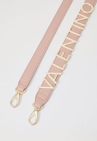 Puha rózsaszín bőr vállpánt, arany tónusú logóval és elegáns kapcsokkal. Simább textúra, minimalista dizájn.