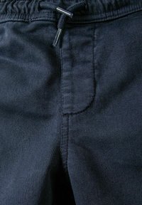 Tmavě modré jogger kalhoty z látky s elastickým pasem, které mají šňůrku a boční kapsy, vyrobené z jemného, texturovaného materiálu.