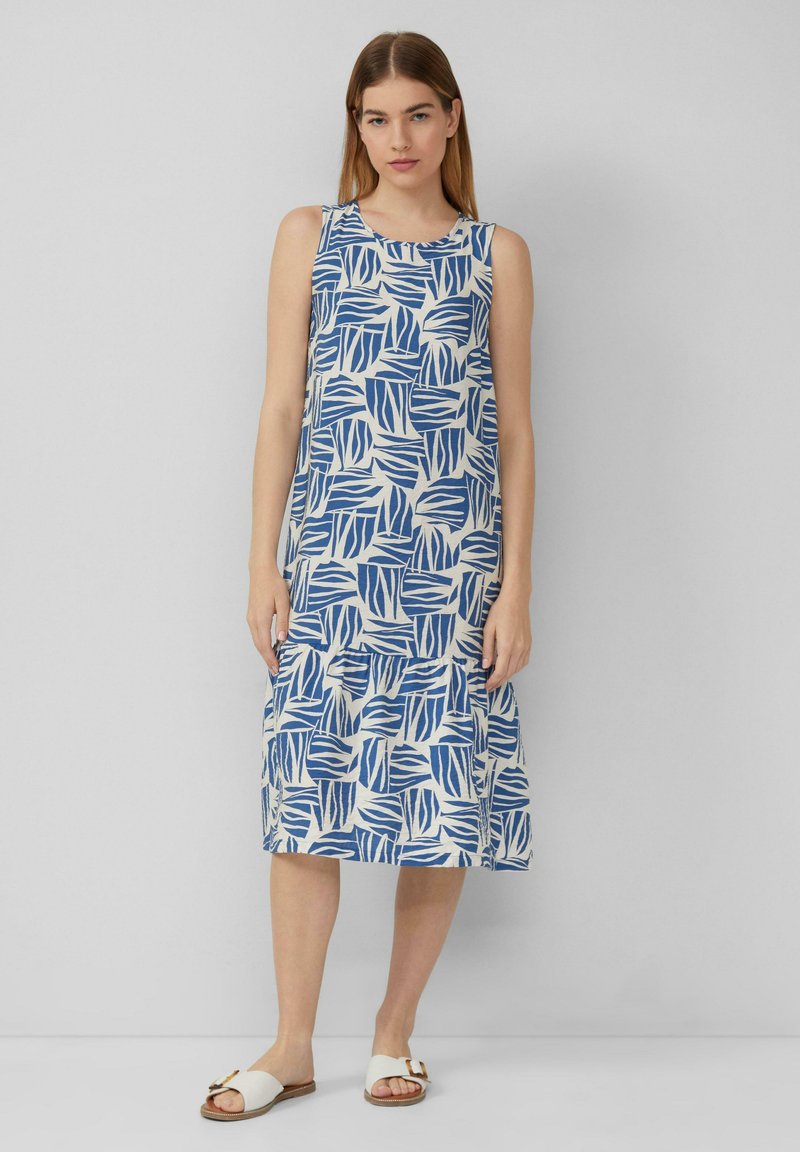 Ärmelloses blau-weiß gemustertes Kleid mit Blattdesigns, gestuften Saum, leinenähnlicher Textur, kombiniert mit hellfarbigen Sandalen.