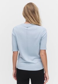 Světlomodrý pletený pulovr s krátkými rukávy, má kulatý výstřih a střední zadní šev s malým knoflíkovým detailem.