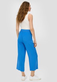 Blauwe wijde broek met een elastische tailleband, gemaakt van lichtgewicht stof, gecombineerd met witte sneakers en een aansluitend geribbeld tanktop.