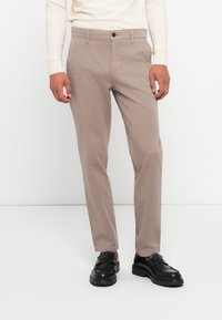 Beige katoenen broek met een slim fit, voorzien van een sluiting met een frontknop, zijzakken en een subtiele textuur. G gedragen met zwarte instappers.