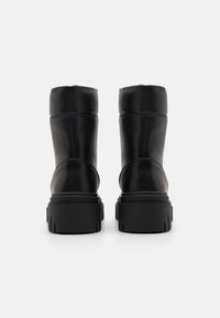 Czarne skórzane botki na kostkę z masywną teksturowaną podeszwą, gładką cholewką i minimalnymi detalami przeszycia, prezentujące prosty i funkcjonalny design.
