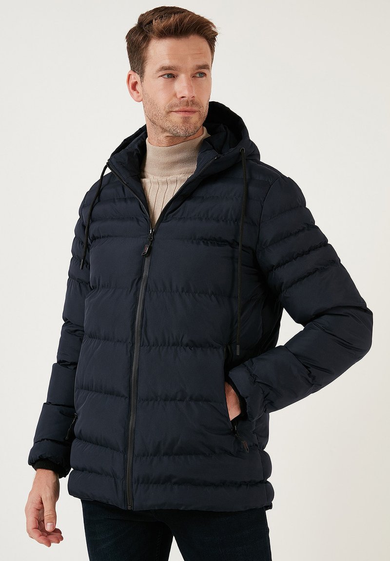 Giubbotto imbottito blu navy con zip frontale, cappuccio e pannelli testurizzati. Include un cordino regolabile e due tasche laterali.