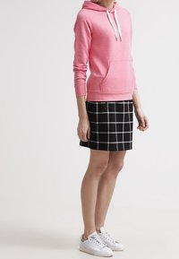 Sweat à capuche rose clair avec poche avant, assorti d'une jupe à carreaux noirs et blancs. Des baskets blanches complètent la tenue.