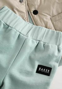 Svetlo béžová prešívaná bunda a mäkké mätovo zelené tepláky s rebrovaným pásom; má čiernu nášivku s nápisom "BAKER."
