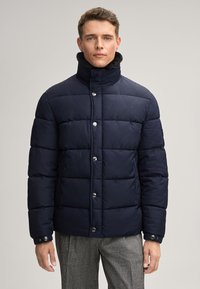 Giacca a vento blu notte realizzata in tessuto imbottito e liscio, con colletto alto e bottoni argentati. Presenta cuciture orizzontali e un design elegante.