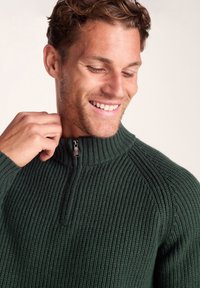 Dark green knitted sweater with a high collar and a half-zip closure, featuring ribbed texture and a fitted design.