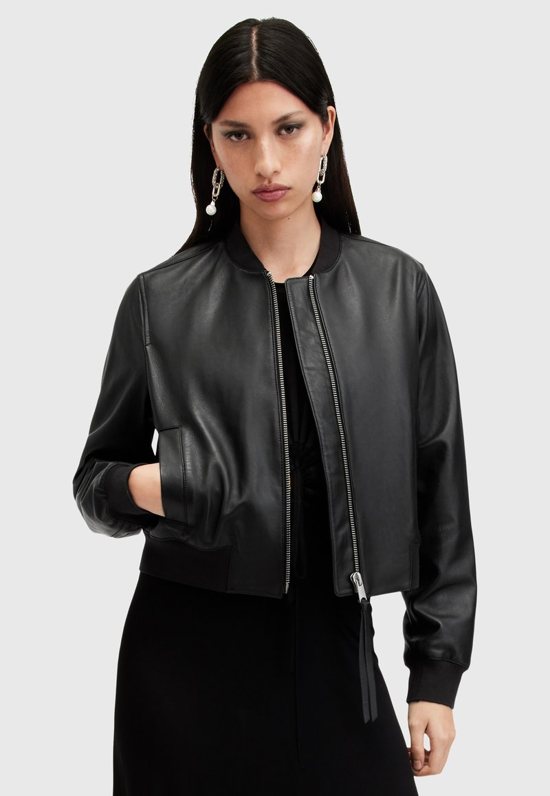 Chaqueta bomber de cuero negro con puños y cuello acanalados. Cuenta con un cierre frontal, bolsillos laterales y un corte corto. Textura suave.