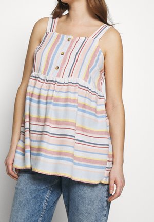 Frau trägt ein ärmelloses, locker sitzendes gestreiftes Oberteil mit Knöpfen vorne, kombiniert mit blauen Jeans.