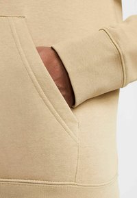 Felpa beige con una texture morbida, dotata di tasca a marsupio e polsini a coste. Tessuto liscio con dettagli di cucitura visibili.