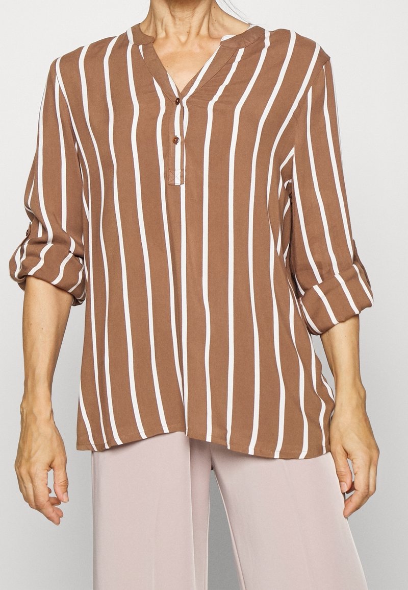 Blouse rayée marron et blanche avec un col en V, des manches trois-quarts et un détail à boutons. Confectionnée en tissu léger avec une coupe décontractée.