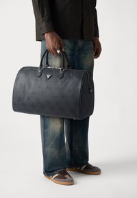 Borsa da viaggio in pelle blu scuro con un delicato motivo a monogramma, forma arrotondata, doppi manici superiori, hardware in tonalità argento e chiusura con zip.