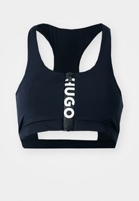 Marine blå sports-bh laget av elastisk stoff med racerback-design, med en frontglidelås og fremtredende hvit "HUGO"-merking.