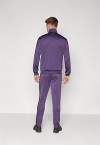 Lilla idrettsdrakt med høy krage, tettsittende design og kontrasterende svarte side-striper på buksene. Glatt tekstur.