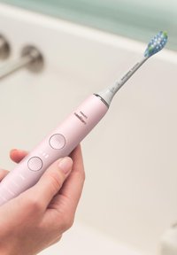 Brosse à dents électrique avec un manche rose, des accents argentés, des boutons d'alimentation et de mode, et une tête de brosse aux poils bleus et verts.
