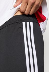 Sorte atletikshorts med tre hvide striber langs siden, lavet af glat stof. En løs pasform i taljen er delvist synlig.