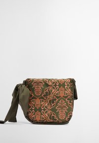Zielona torba na ramię z materiału w kwiatowy wzór w kolorze pomarańczowym. Posiada zapięcie nawiązujące oraz zaokrąglony kształt. Teksturowana powierzchnia z błyszczącym wykończeniem.