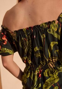 Rochie off-the-shoulder din material închis, cu modele de frunze verzi și flori. Dispune de un brâu elastic și mâneci scurte, creând o siluetă relaxed.
