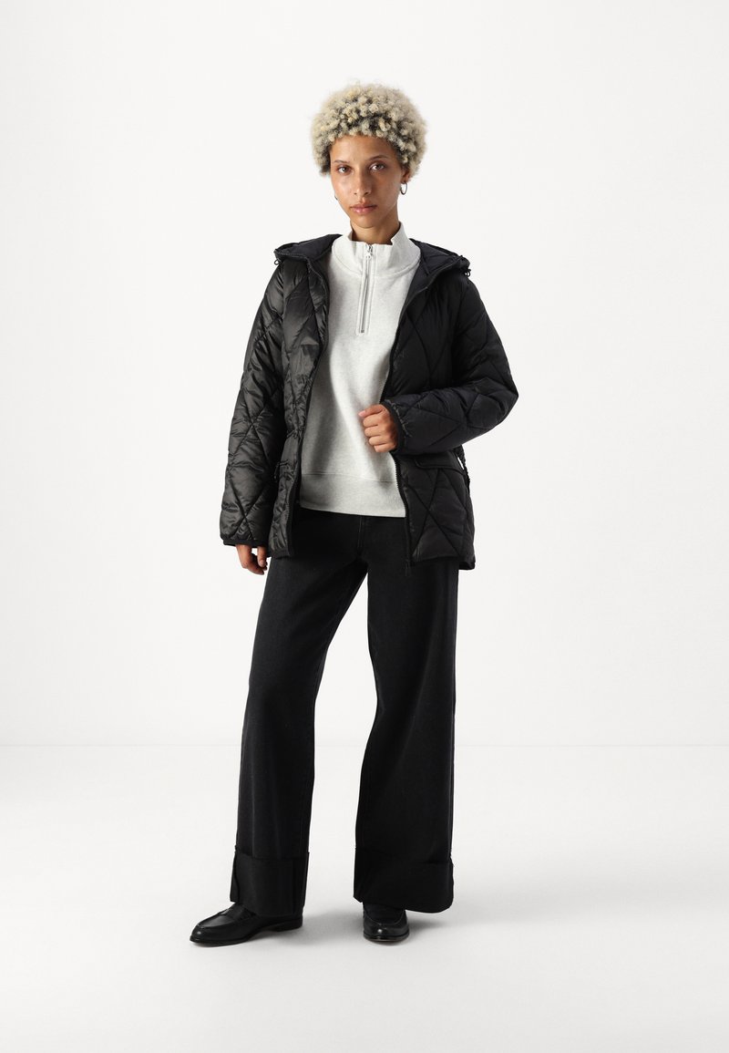 Chaqueta acolchada negra con capucha y cierre frontal de cremallera, combinada con un forro polar gris claro de medio cierre y pantalones anchos negros. Textura suave.