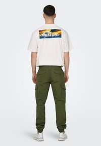 Weißes T-Shirt mit einem farbigen Grafikmotiv auf der Rückseite, das mehrfarbige Wellenmuster und den Schriftzug "ONLY&SONS" zeigt; grüne Cargo-Hose mit elastischen Bündchen.