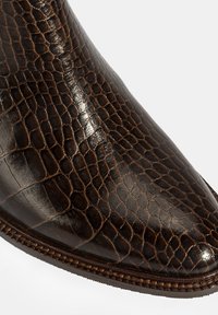 Braune Lederstiefel mit glanzvollem, strukturiertem Krokodilsmuster, spitzem Zeh und detaillierter Naht entlang der Sohle.