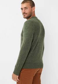 Grüner Strickpullover mit strukturierter Oberfläche, Rundhalsausschnitt und gerippten Bündchen, kombiniert mit braunen Cordhosen.