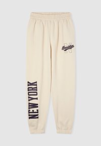 Beżowe dresy z elastycznym pasem, z nadrukiem "NOWY JORK" w granatowym kolorze na jednej nogawce oraz "Brooklyn" z ozdobną literą na drugiej.
