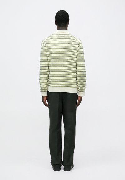 Lichtgroene gebreide trui met horizontale strepen, gecombineerd met donkergroene broek. Voorzien van geribbelde manchetten en een eenvoudig kraagontwerp.