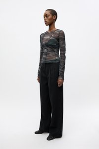 Long-sleeve, sheer top with a fitted design in dark green, featuring scalloped neckline and textured fabric, paired with wide black trousers.