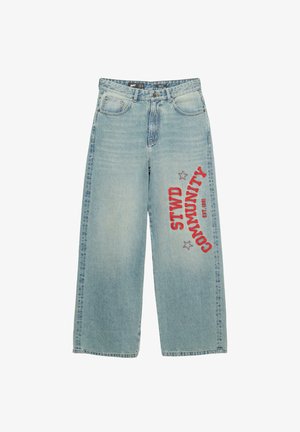 Svijetloplavi, široki traperice s izblijedjelom teksturom, sa crvenim otisnutim tekstom "STWD COMMUNITY" i zvjezdicama na desnoj nozi.