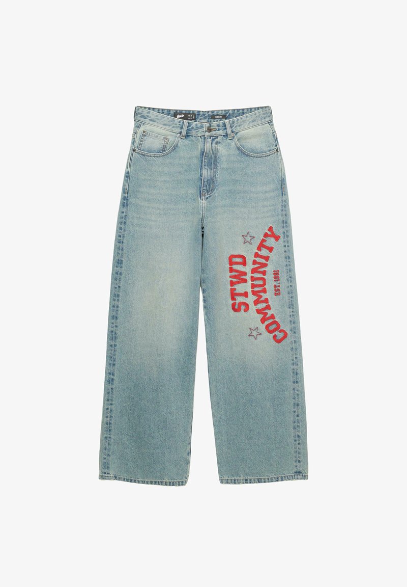 Jeans in denim azzurro chiaro con gamba larga e texture sbiadita, caratterizzati da testo stampato in rosso "STWD COMMUNITY" e stelle sul lato destro.