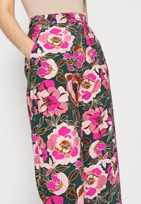 Květinové široké kalhoty v tmavě zelené látce, zdobené velkým vzorem růžových a hnědých květin, se bočními kapsami a zapínáním na knoflík.