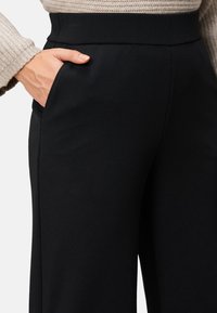 Czarne, dopasowane spodnie o gładkiej fakturze, z kieszeniami po bokach i wysokim pasem. Tkanina jest elegancka i dopasowująca się do sylwetki.