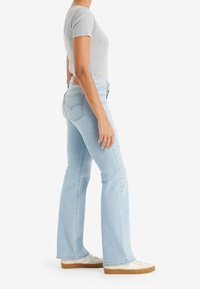 Lätt blå utsvängda jeans med hög midja, gjorda av denim. Har en bakpatch med etikett och något fransade fållar, ihop med vita sneakers.