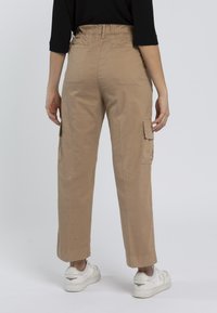 Pantaloni cargo beige con vita elastica, dotati di tasche laterali e design a gamba dritta. Abbinare delle sneakers bianche completa il look.