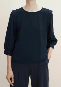 Top blu navy con scollatura rotonda e maniche a tre quarti elasticizzate. Tessuto texturizzato, con una vestibilità comoda. Abbinato a pantaloni scuri.