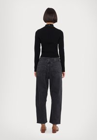 Svart, ribbad långärmad tröja i kombination med högmidjade, mörkgrå vida jeans. Anmärkningsvärda detaljer inkluderar bakfickor och en dragkedja vid halsen.