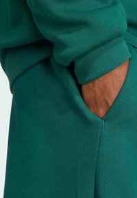 Grön sweatshirt med ficka, med en mjuk textur, ribbade muddar och en avslappnad passform, som visar en ren design och sömlös sömnad.