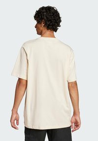 Maglietta in cotone color crema con maniche corte e collo rotondo. Presenta una vestibilità morbida e un design minimalista, con evidenza della trama naturale del tessuto.