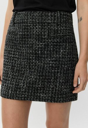 Black and white tweed mini skirt featuring a textured fabric, structured shape, and a smooth waistband. Ideal for versatile outfits.