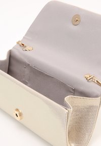 Lille elegant beige clutch-pung med lysegrå stofindvendig, der har guld magnetlås og kædevedhæftninger.