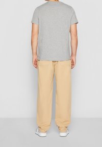 T-shirt grigia a maniche corte, pantaloni beige a gamba larga e sneakers bianche. Look casual con un design semplice e morbido tessuto di cotone.