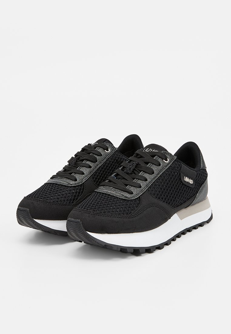 Chaussures de sport noires avec tige en mesh et en suède, accents gris, lacets ronds et semelles blanches présentant un motif de traction texturé.