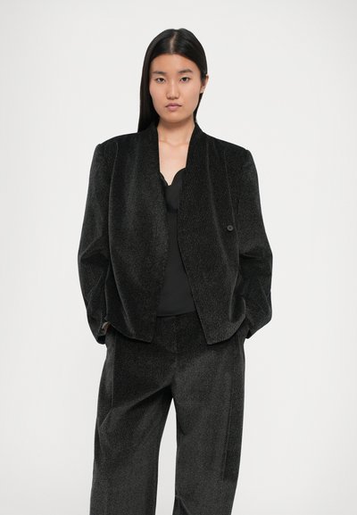 Blazer noir texturé avec une coupe décontractée et un léger éclat, associé à un top noir et un pantalon assorti. Conçu sans attaches visibles.