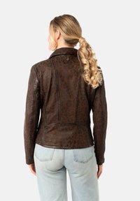Chaqueta de cuero marrón con un patrón de leopardo, diseño ajustado, detalles de costura sutiles y un cuello clásico. Combinada con unos vaqueros azul claro.